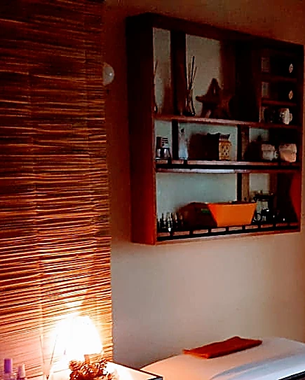 Repisa de madera con aromatizantes y objetos decorativos sobre una lámpara de sal encendida en la cabina de masaje