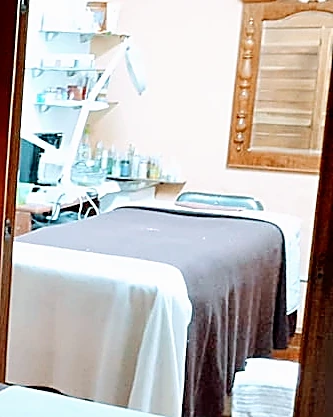Sala de faciales: camilla con cubierta blanca y café, lámpara de aumento y repisas con productos