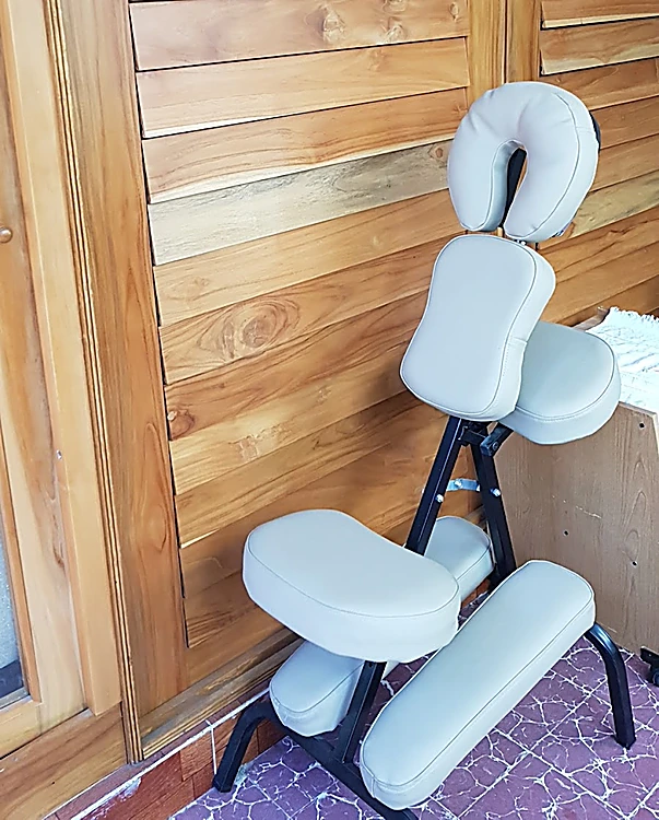 Silla de masaje gris claro, lista para usarse, frente al muro de persianas de teca